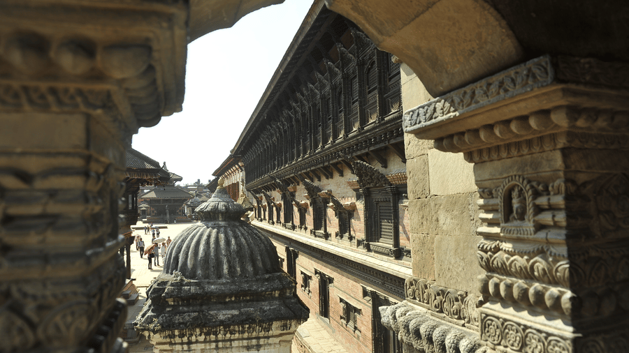 Scenic view of traditional carved Newar temple roofs framed through an ancient stone archway in Patan, Nepal.