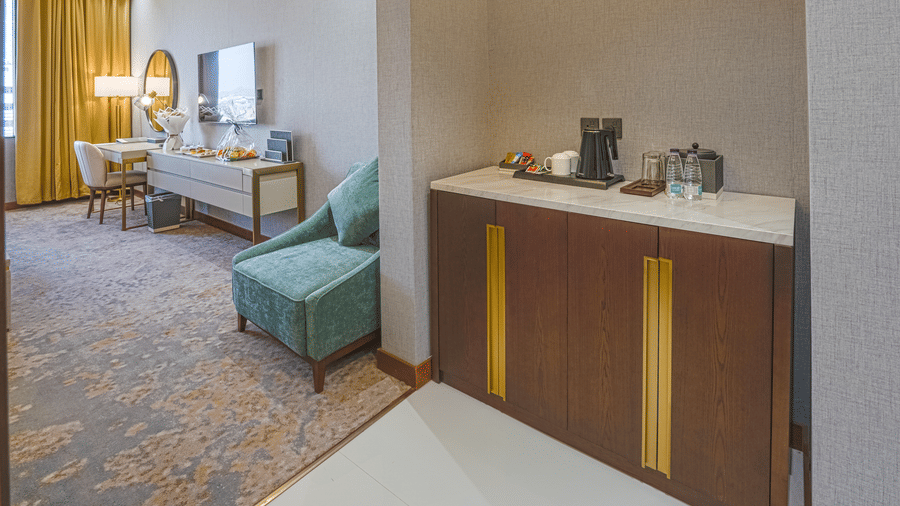 Vanity shelf seen with a tea & coffee maker on top, and a wa short wall partition separating it from the seating area and TV shelf in a Standard King Room at Grand Iva Hotel, Abha.