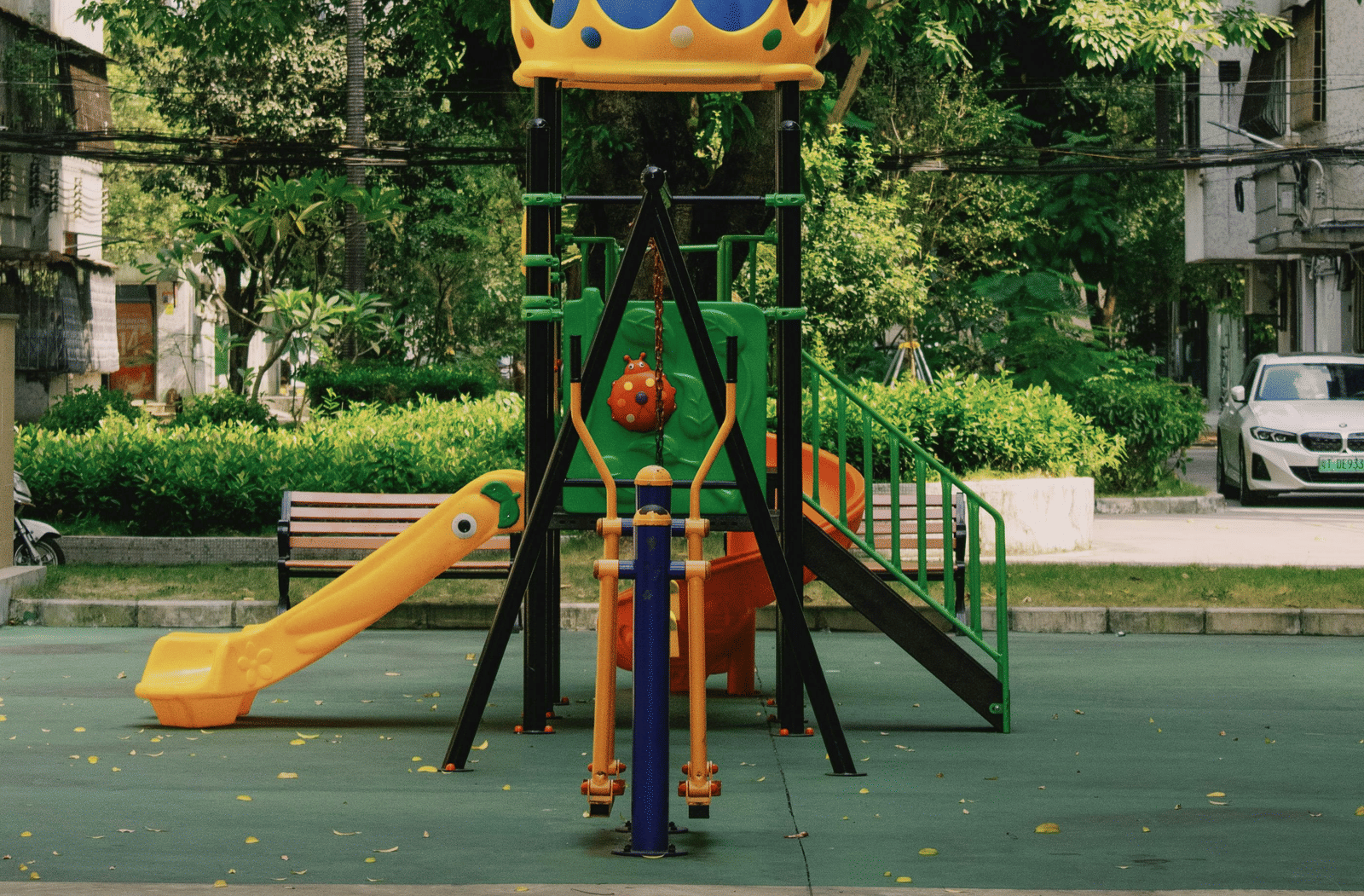 A colourful children's playground structure stands prominently beneath a large, leafy green tree.