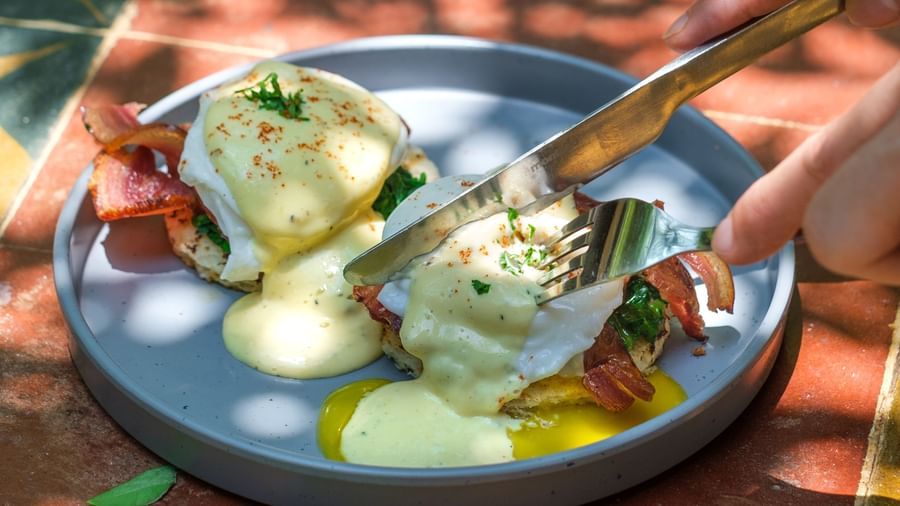 A person digging into a plate of Eggs Benedict | Mango Hill, Pondicherry