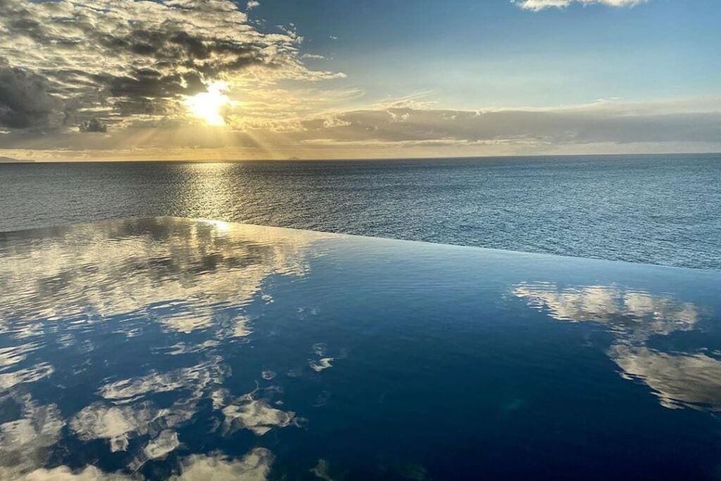 A sunset/sunrise in the ocean featuring an infinity pool that mirrors the sky.