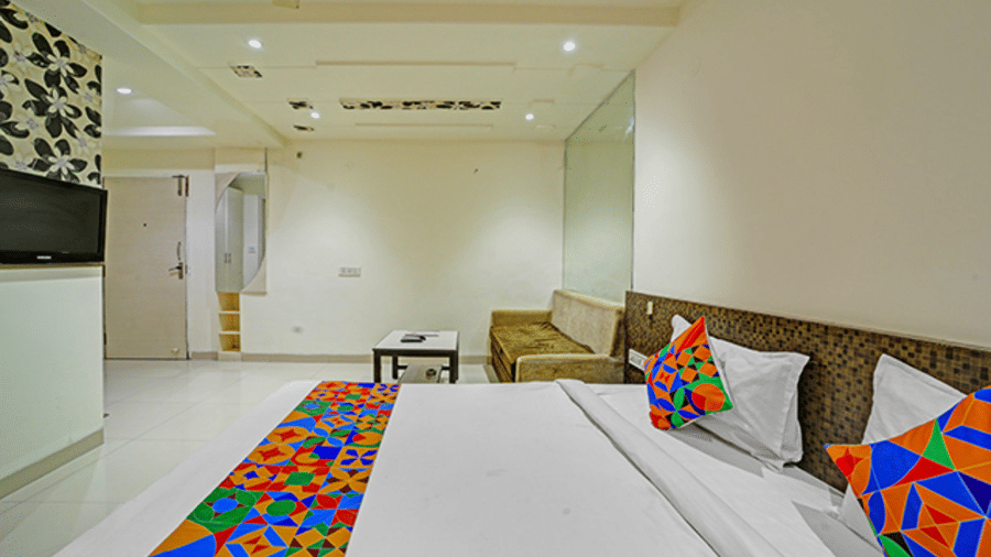 Twin beds with long colorful runner, sofa seating, TV and bright ceiling lights at Hotel Maurya, Bhopal.