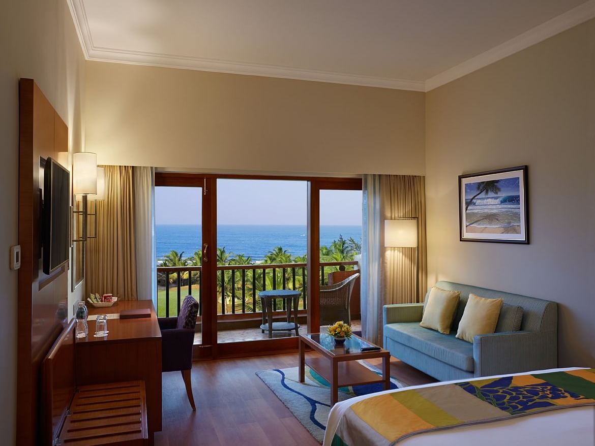 a double bed with a sofa, table, lamps and tv in view inside Ocean front view - Caravela Beach Resort Goa