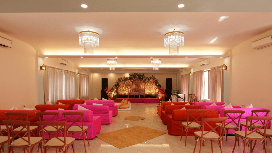 An illuminated event hall at Grassfield Riviera Resort, featuring chairs, sofas, chairs, facing the stage decorated with floral theme , chandeliers, and windows covered with curtains.