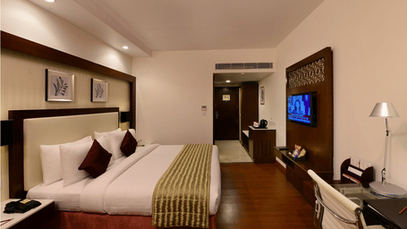 A room with double bed, side table,TV, work desk, lamp, decor frames and chair