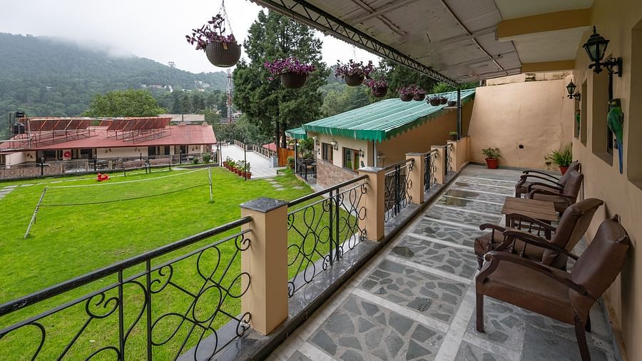 Covered balcony at The Pavilion, Nainital with wooden seating, decorative iron railings, and panoramic views of the lush green valley below.