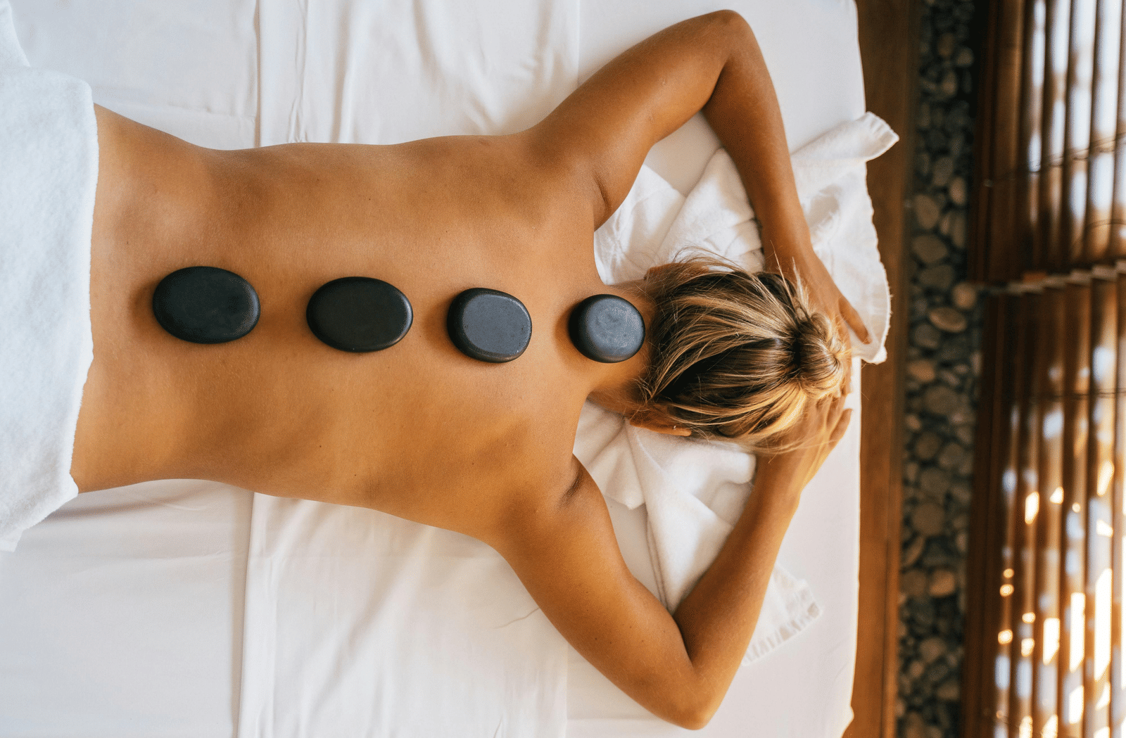 A woman lying down with back with black stones kept over her spine.