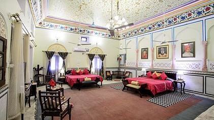 A large suite at The Umaid Vilas Jaipur with two beds dressed in red linens, a patterned ceiling, and traditional Indian decor.