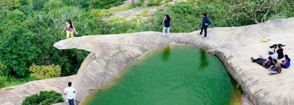 A small green-coloured lagoon on a rock platform at Avalabetta in Bengaluru, with several people surrounding it enjoying the views fro the hill top.