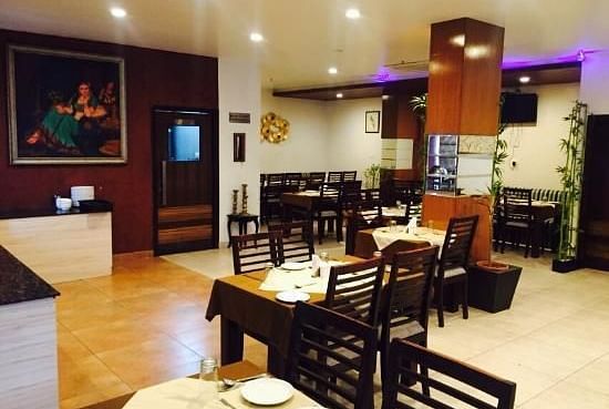 An elegantly set dining area with wooden chairs and tables, under ambient lighting and a painting on the wall - TGI Apple Inn, Jaipur 