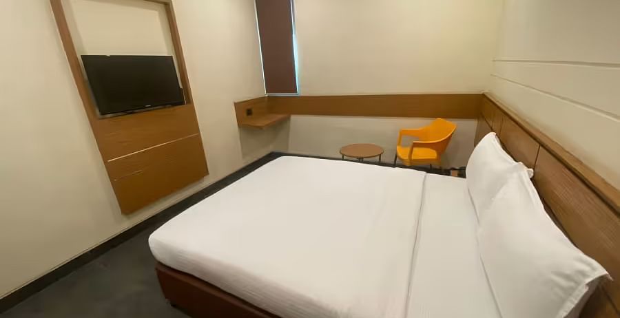 A simple, clean hotel room featuring a double bed, a wall-mounted TV, and basic furnishings- Max Hotel Prayagraj.
