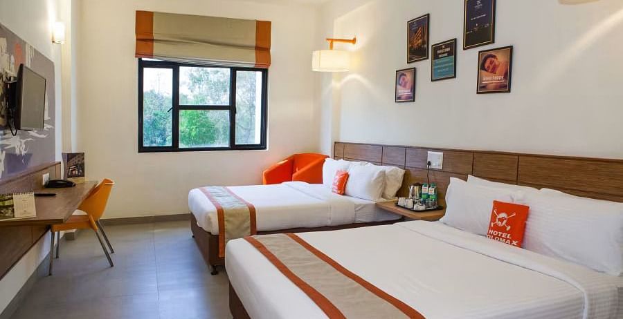 View of two beds arranged in a hotel room with a large window and natural lighting- Max Hotel Prayagraj.