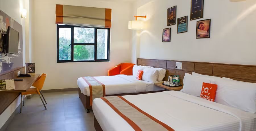 View of a hotel room featuring two comfortable beds, wall art, and a large window with natural light - Max Hotel Prayagraj.