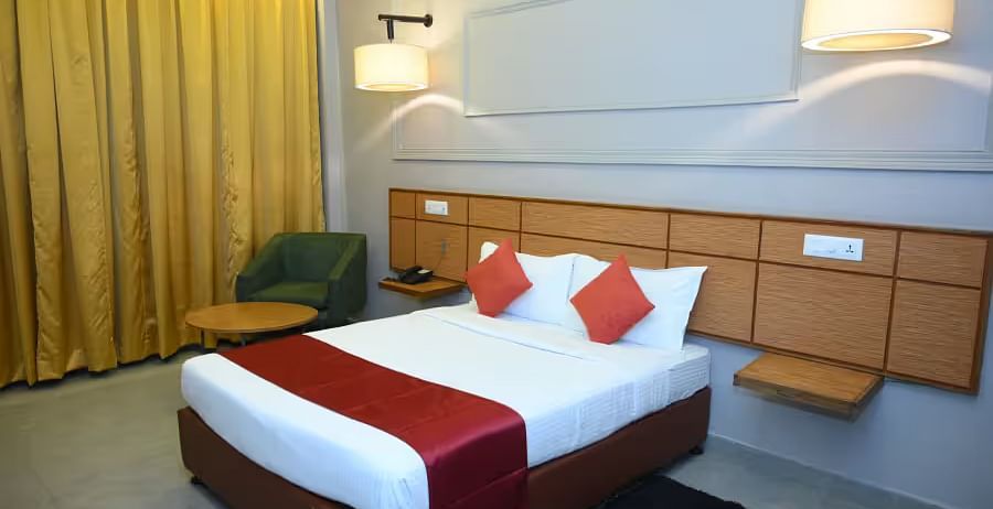 A well-designed hotel room with two beds, modern lighting, and a cosy seating area - Max Hotel Prayagraj.