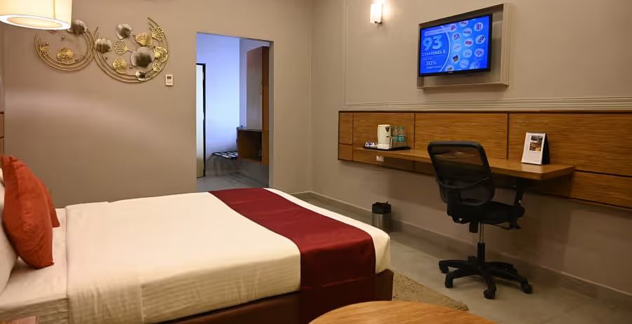 View of a neat hotel room featuring a bed, a wall-mounted TV, a work desk, and warm lighting - Max Hotel Prayagraj.