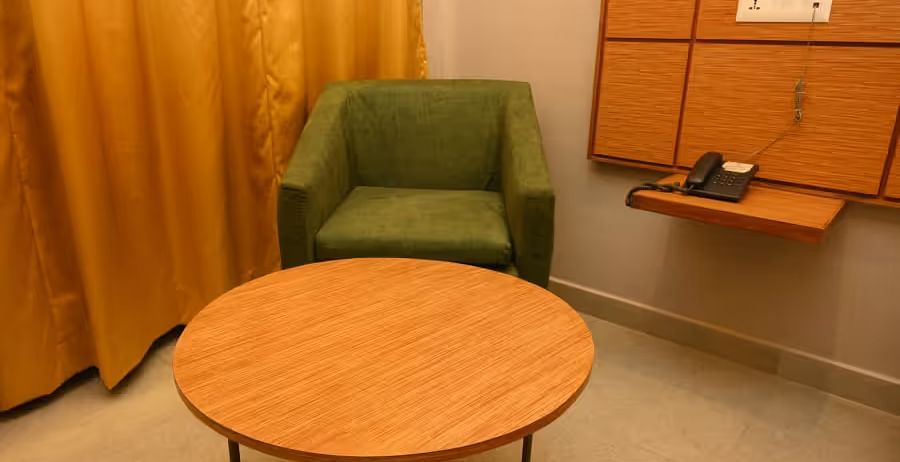  A cosy seating space with a round wooden table and a comfortable green armchair - Max Hotel Prayagraj.