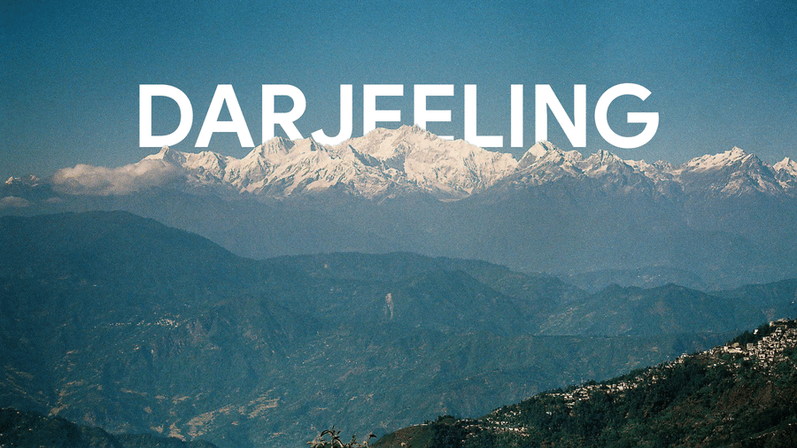 Scenic view of Darjeeling one of the best places to visit in North Bengal with snow capped Himalayan peaks layered green hills and bold Darjeeling text overlay across the sky