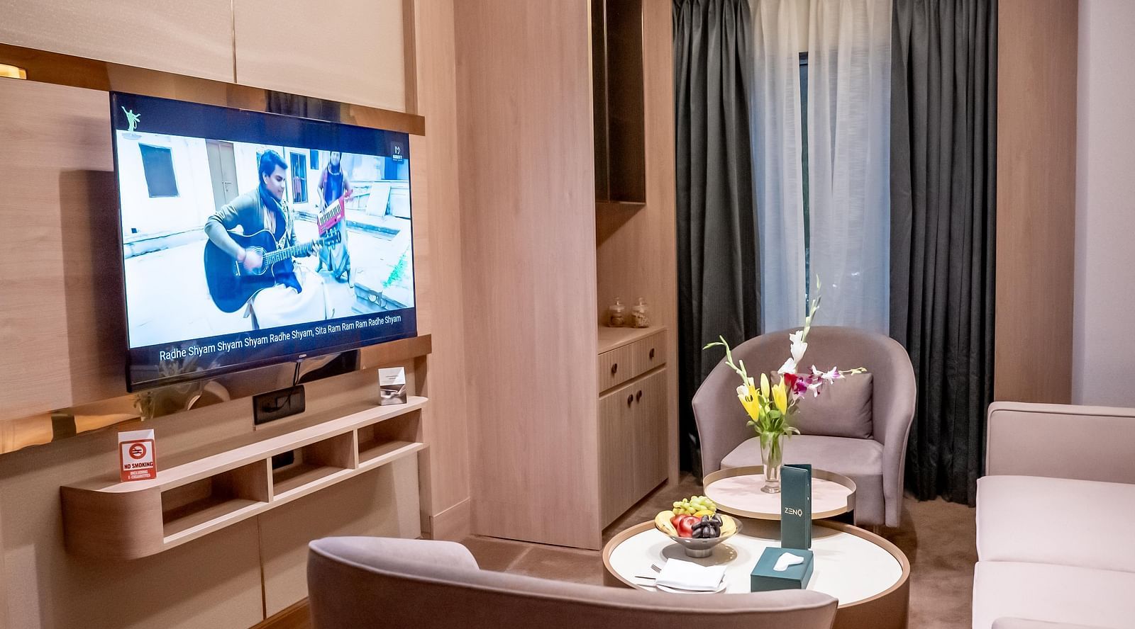 Living room set up with sofa, chairs, wall mounted TV and window with a curtain in the background at ASTER GRAND BY ZENQ SAKET.