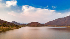 a lake near sariska palace in alwar with small hills in the background.