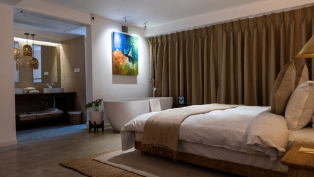 A spacious room with bed, bathtub, wall hanging and the washroom area at the Nepali Suite - The Nanee