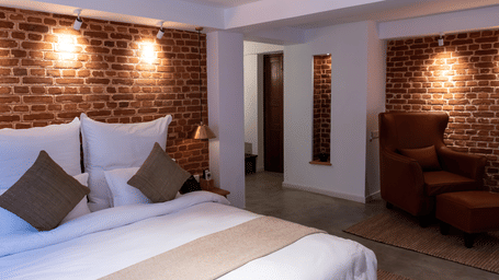 The Nepali Suite featuring a bed with pillows and cushions, sofa and walls of bricks depicting the element of earth - The Nanee
