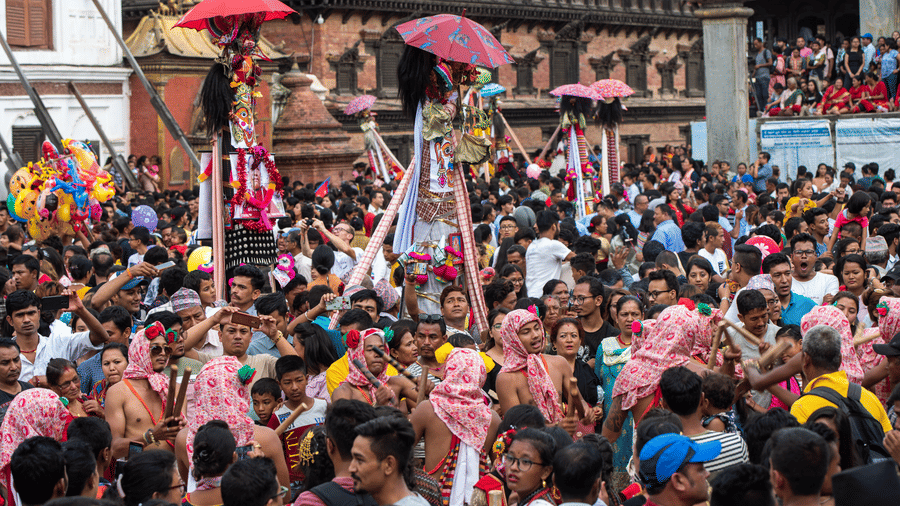 A large crowd of local residents parading with tall umbrellas and wooden poles down the heritage streets of Bhaktapur, Nepal.