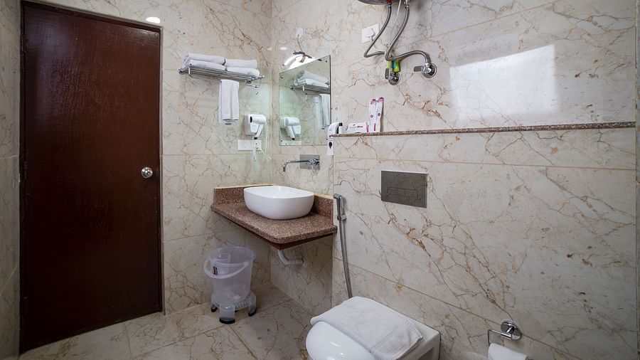 Sumitel Hotel's bathroom with beige marble tiles, a wall-mounted sink, toilet, bidet shower, and shower area.