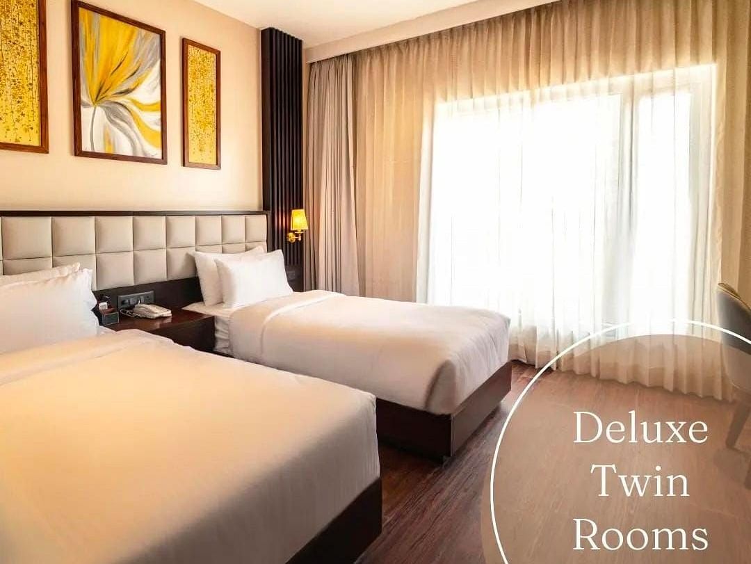 A image of a room with twin beds and lights seeping into the room from a window