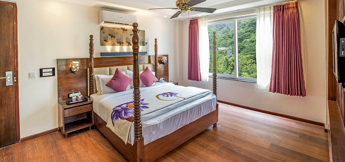 A comfortable double bed with a ceiling fan right above it on a false ceiling and a window besides it at Regenta Inn DLS.