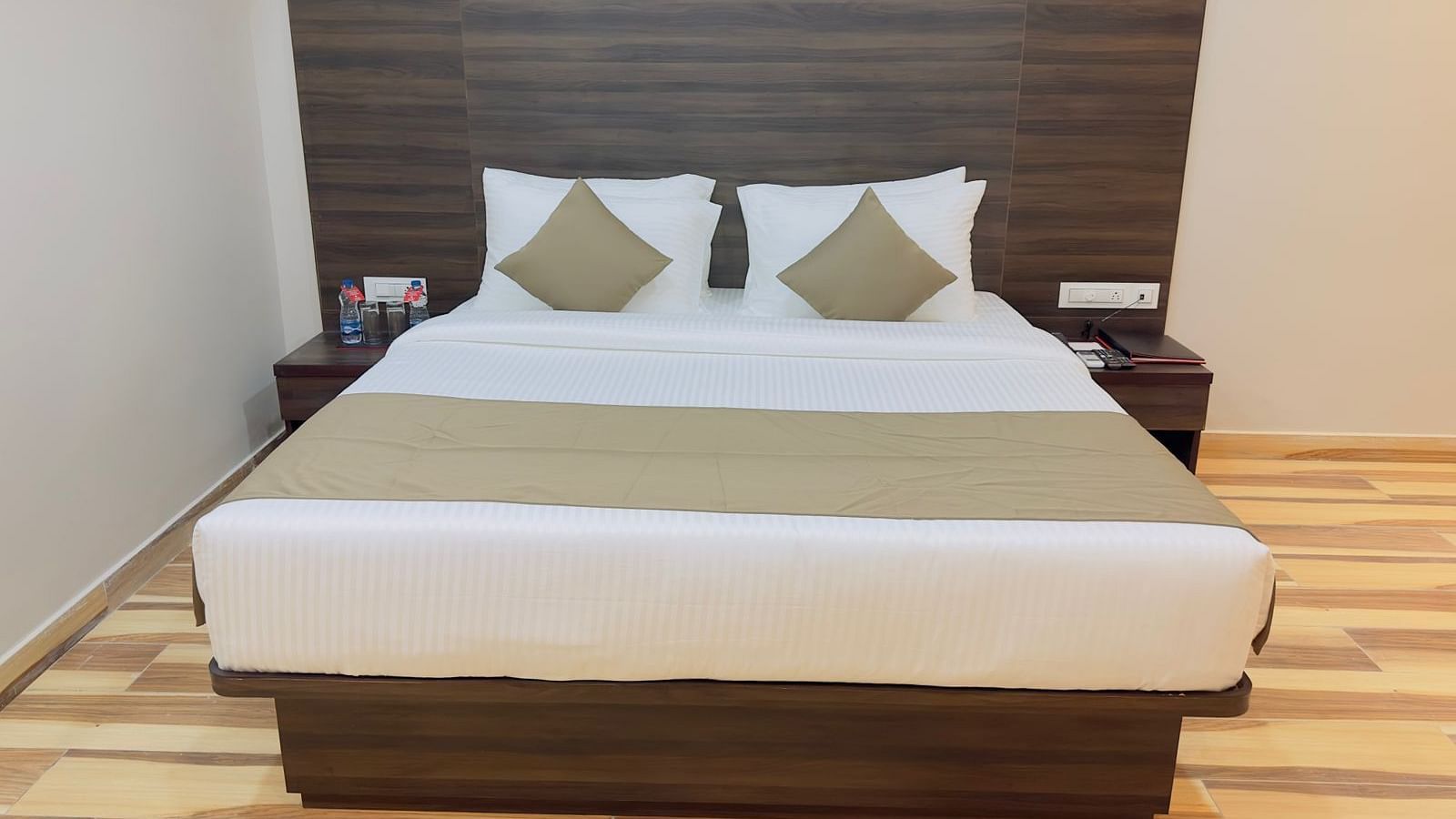 A close-up of a double bed with beige and white linens and a dark headboard - Kankidham Lords Inn