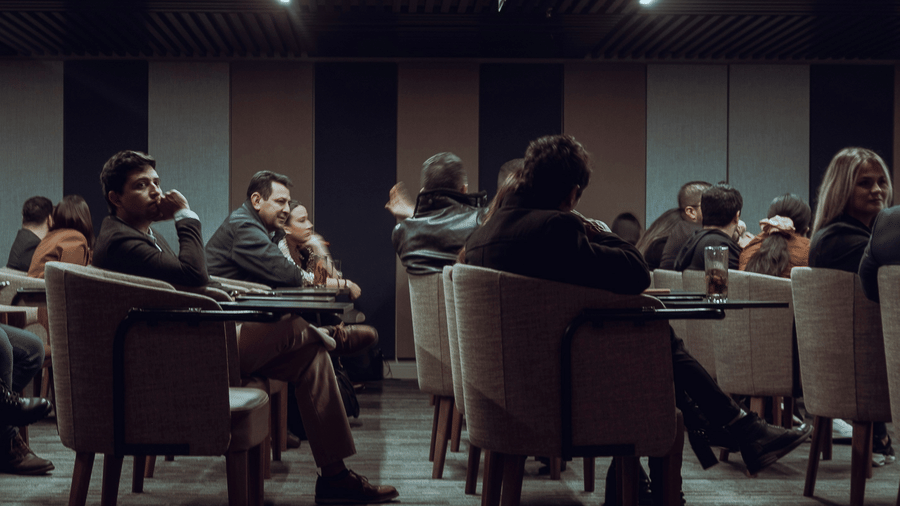 A group of people seated in a conference room, attending a seminar or business discussion, with some attendees engaged and others listening attentively.