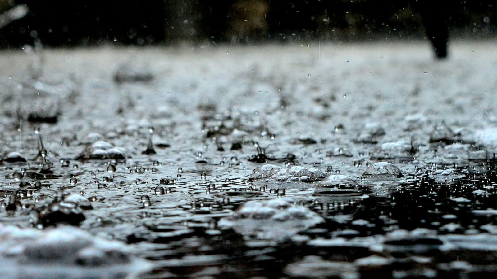 Close up of heavy raindrops splashing on a wet surface, creating ripples and blurred reflections.