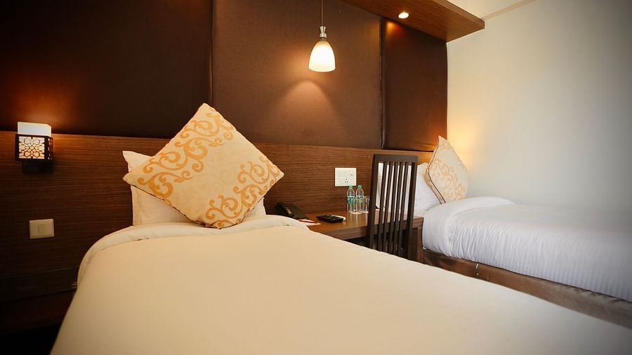 A bedroom with a neatly made bed, decorative pillow, and a wooden headboard with a lamp - VITS Gurugram