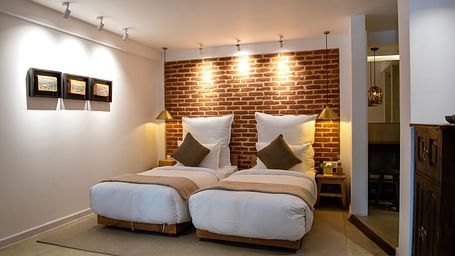 The room at The Nanee includes twin beds, bedside tables with lamps, and three pieces of artwork displayed on the wall.