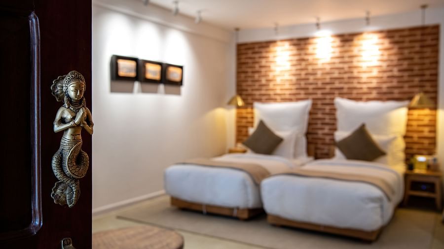 An ajar door with brass handles leading to a room with twin bed - The Nanee