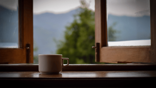 a coffee mug placed on a table by an window that has views of hills and greenery