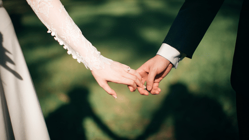 A close-up of a couple holding hands, elegantly dressed in their wedding attire.