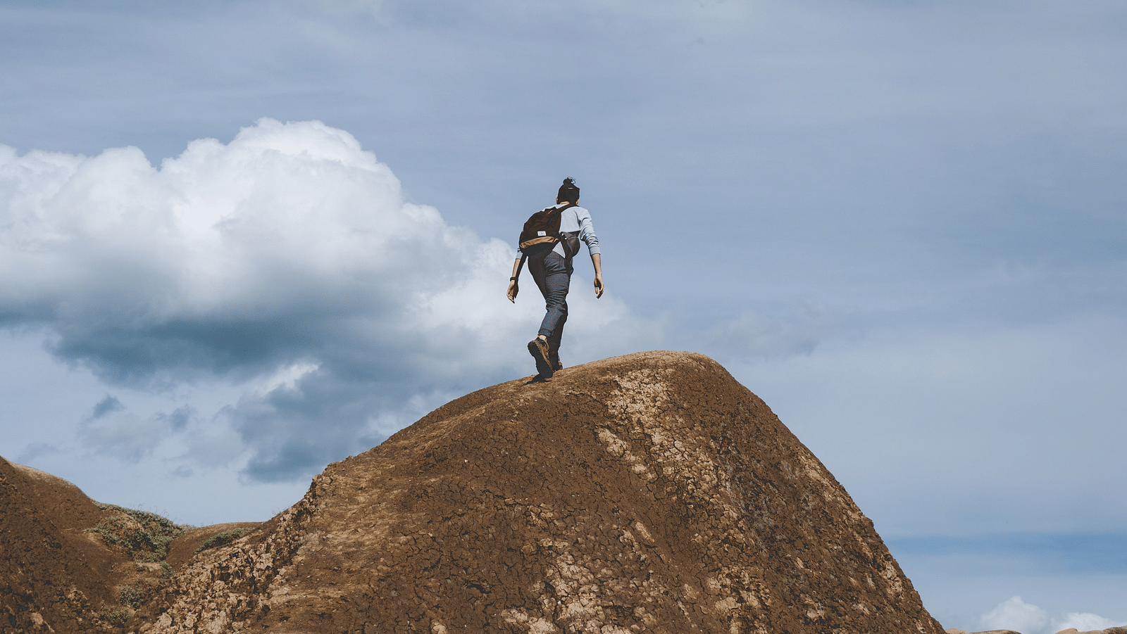 an image of a woman trekking over a cliff with white clouds in the background