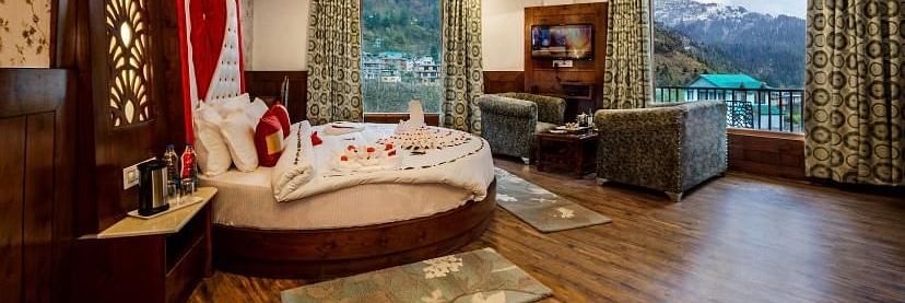 A spacious and luxurious hotel room with a round bed, plush seating, a balcony overlooking a scenic view, and elegant decor | DLS La Serene Manali