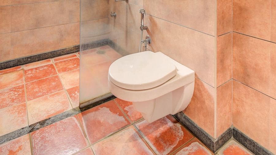 A spacious washroom at Harigovinda's JNStay with a western toilet and a glass panel separating the shower area