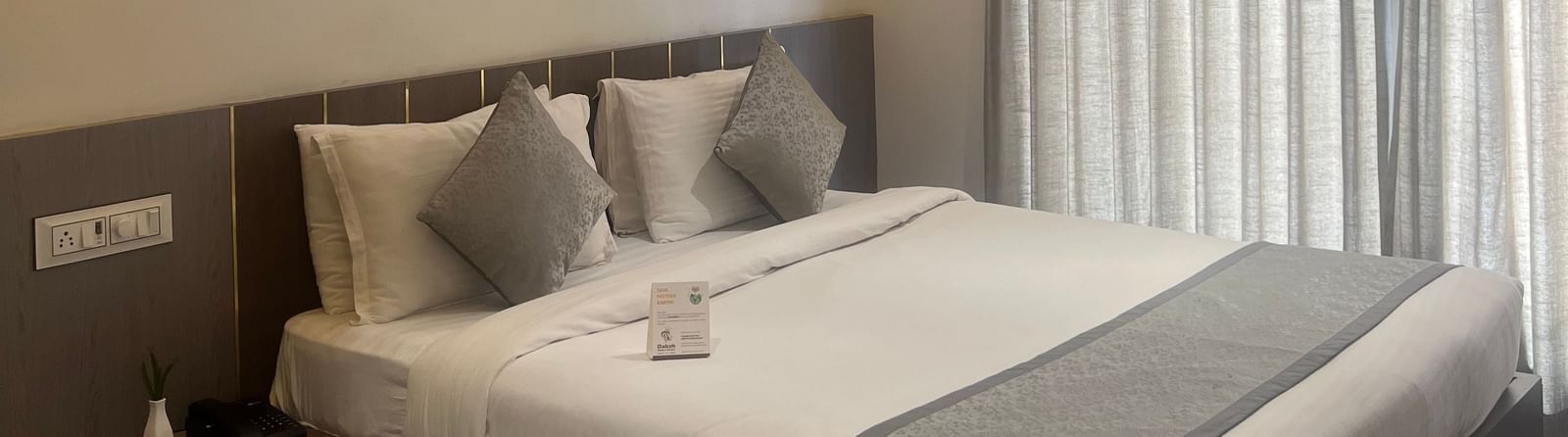 Focus on the double bed in the Daksh Comfort Room at Daksh The Valley Resort, Saputara, seen beside long closed curtains on one side of the room.