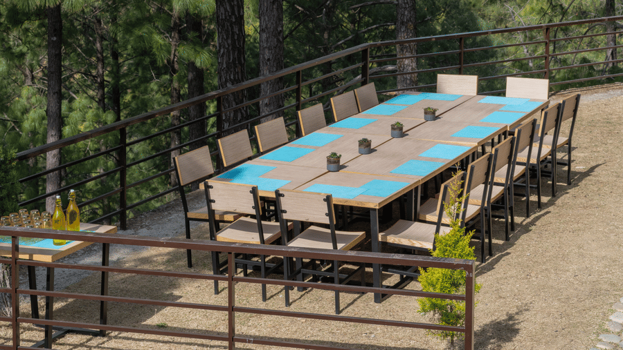 A long dining table with chairs is set up on an outdoor terrace at BluSalzz Escapade Resort, Lansdowne. Trees surround the area.