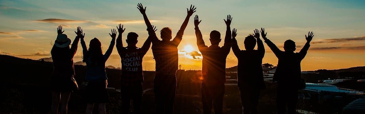 A silhouette of a group of people with raised hands, while watching the sun - Avianna Group of Hotels & Resorts