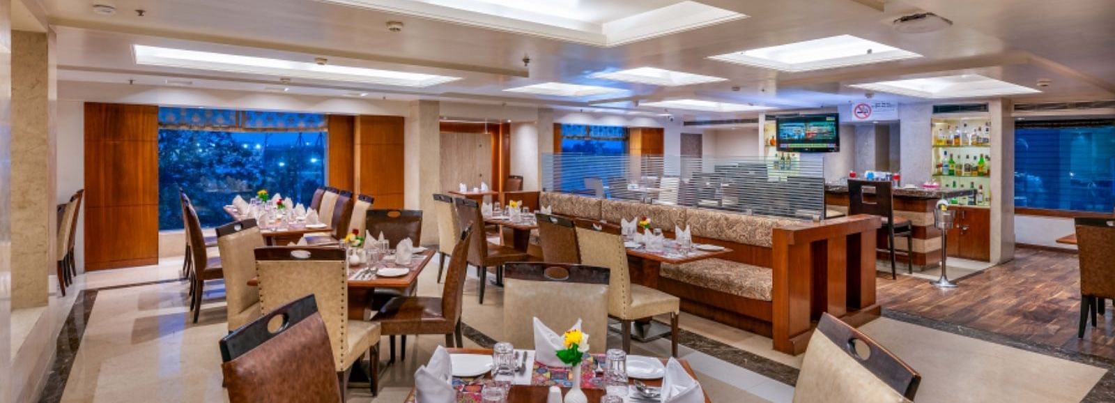 Blue Coriander Restaurant with four and six seaters and a bar counter with a wall mounted TV at Libra Lords Inn Jaipur