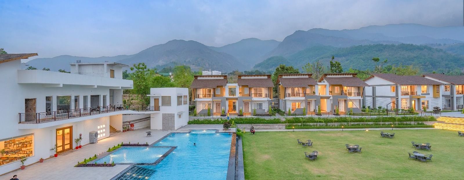 An aerial view of a luxury resort with a swimming pool, surrounded by lush greenery and mountains in the background.