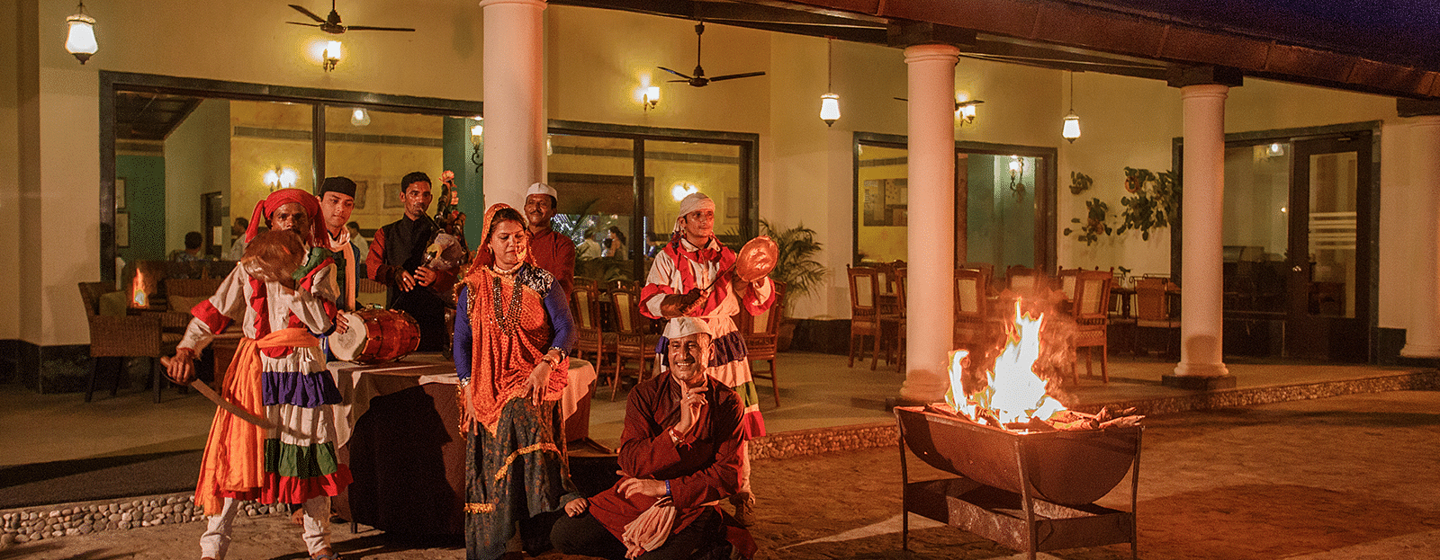An image of a group of people in traditional clothes dancing and playing musical instruments near a bonfire 