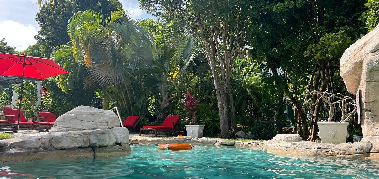 A pool surrounded by rocks, greenery, and red umbrellas | A Stone's Throw Away