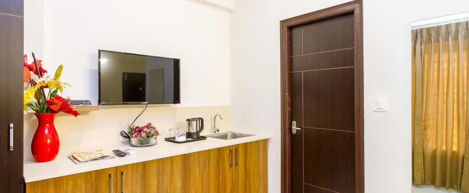 A room showing wooden cabinets, a television, and a closed dark door at Sanctum Suites Whitefield, Bangalore.