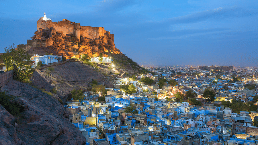Mehrangarh Fort at dusk dominates the Jodhpur city, where blue-painted buildings glow beneath the hill.