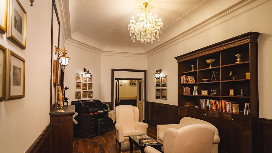 Elegant library lounge with plush white chairs and bookshelves under a sparkling chandelier at The Claridges Nabha Residence